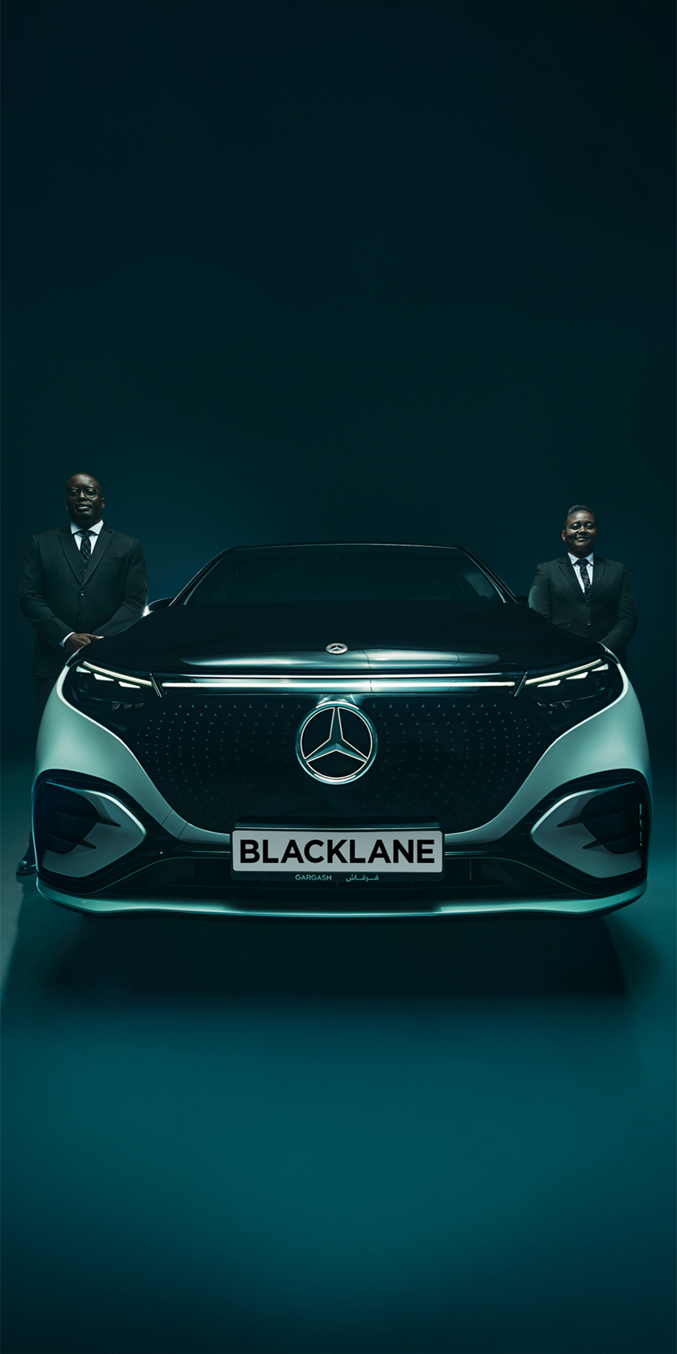 Two chauffeurs stand on each side of a two-toned Mercedes EQS.
