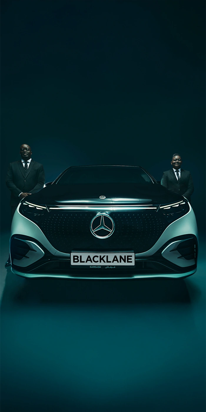 Two chauffeurs stand on each side of a two-toned Mercedes EQS.