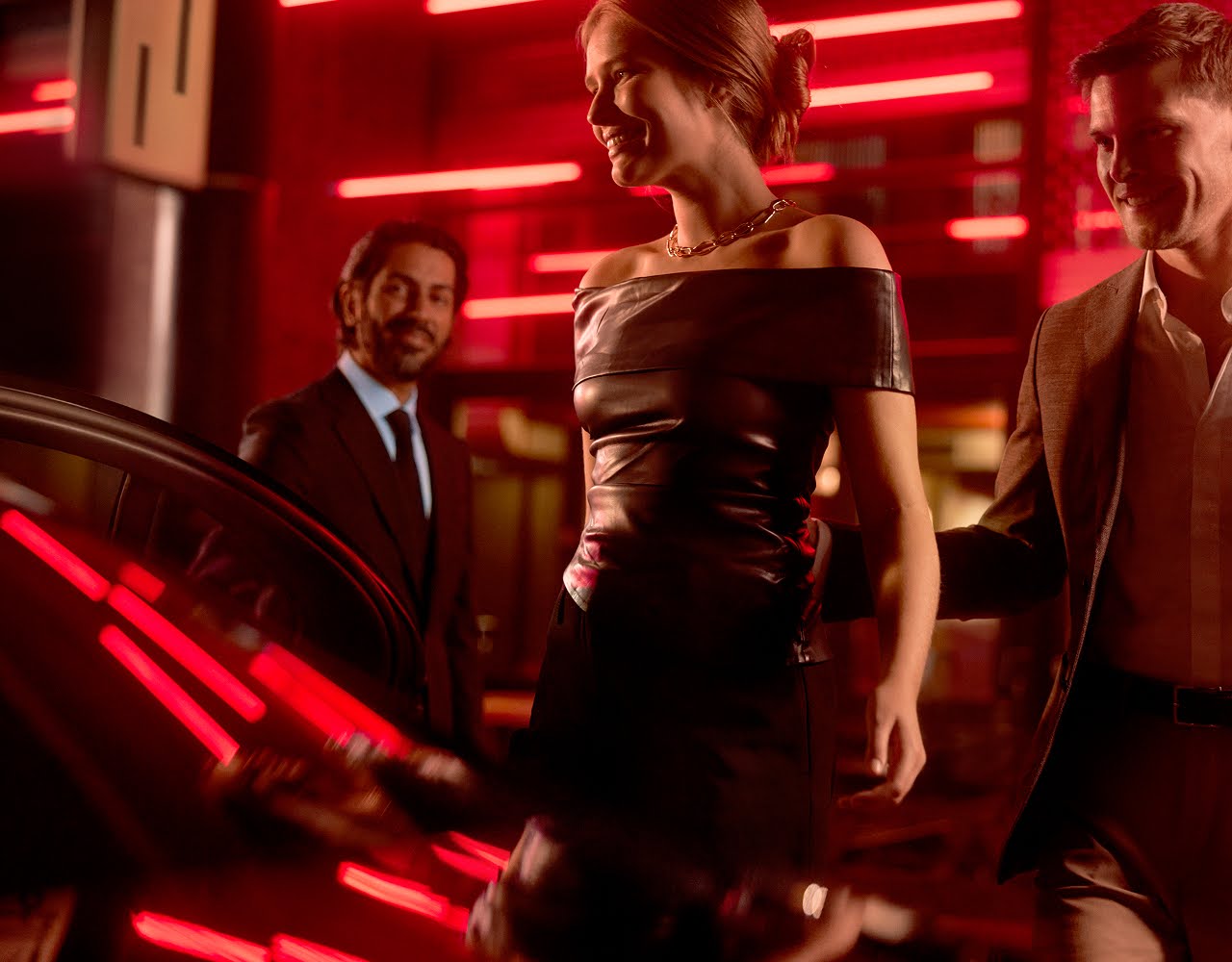 A glamourous young woman and her partner get into a limo as the chauffeur holds open the door.