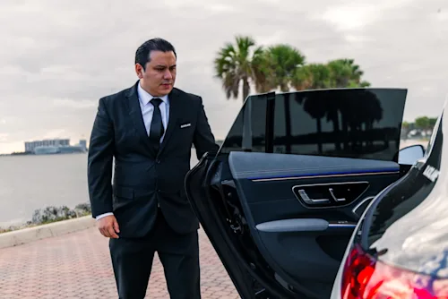 A Blacklane chauffeur in Miami opens a limo door with the sea and palm trees in the background.