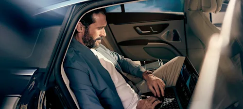 A businessman works on his laptop in the back seat of a Blacklane car.
