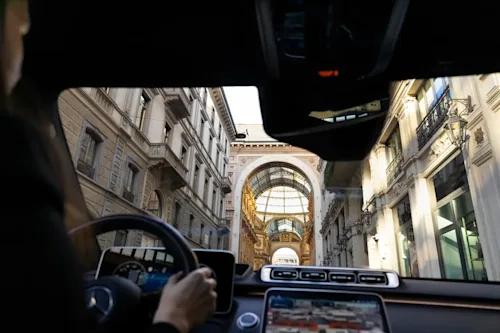 A view of the shopping centre in Milan shot from the backseat of a chauffeured limo, with the dashboard and chauffeur partially in view.