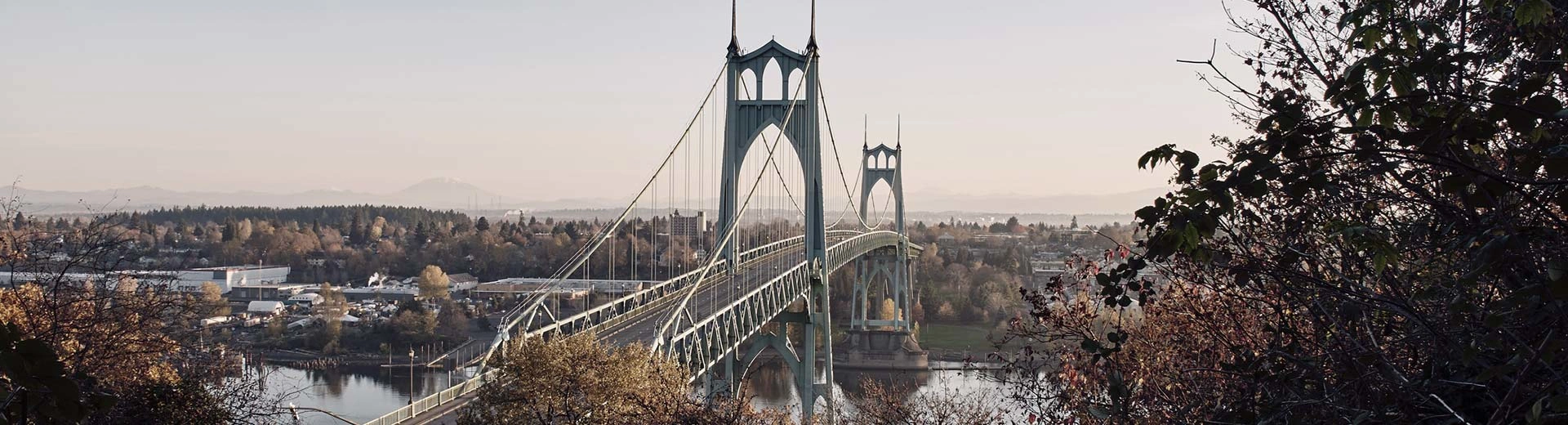 A suspension bridge stretches across a river in Portland, with plenty of trees and green space