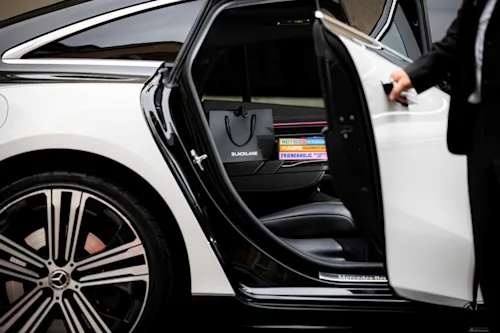 Shot of the Chelsea Curated goody bag through the door of a Blacklane Mercedes EQS with a chauffeur holding the door.