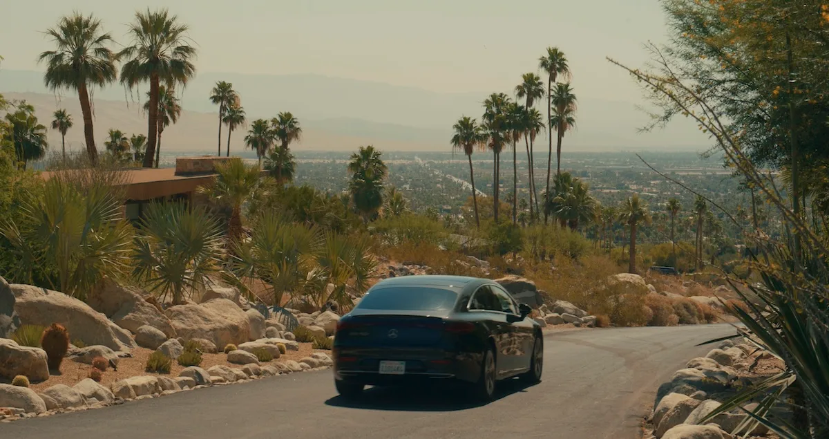 A Blacklane chauffered limousine drives down a street lined with palm trees in a desert town in the American West.