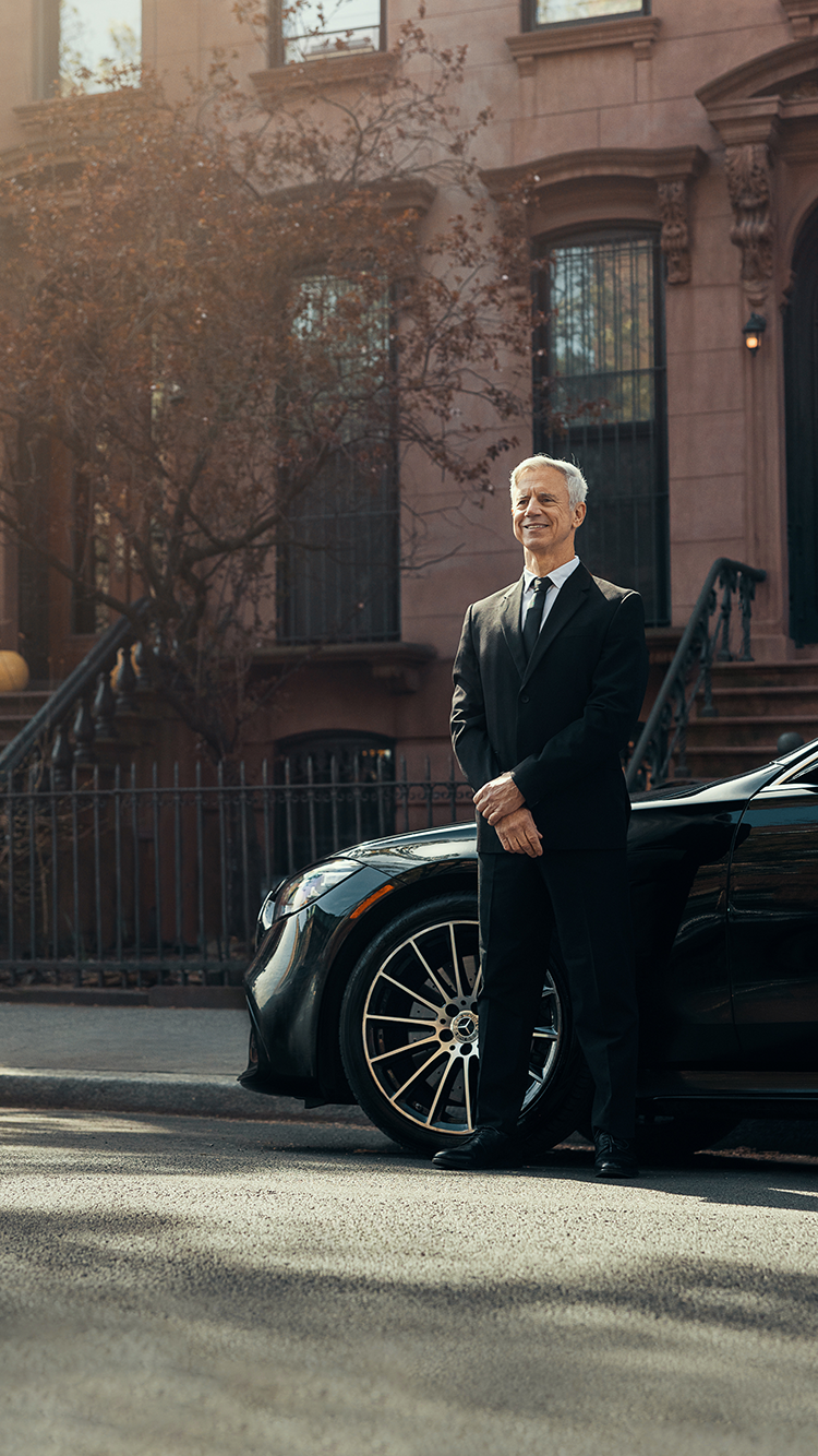 A chauffeur stands next to their vehicle on a clear and bright day.