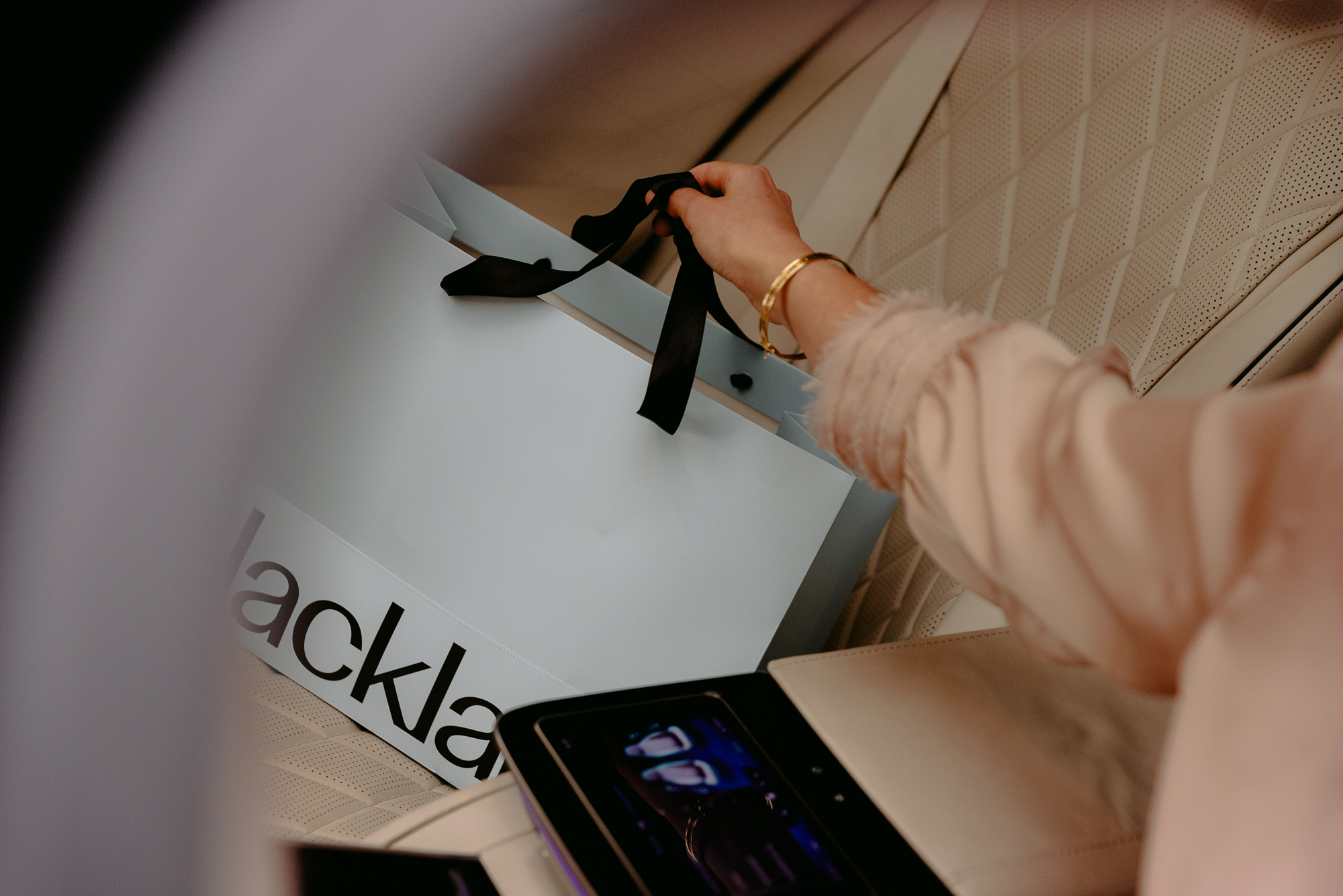A hand holds a Blacklane gift bag in the back seat of a Blacklane limo.
