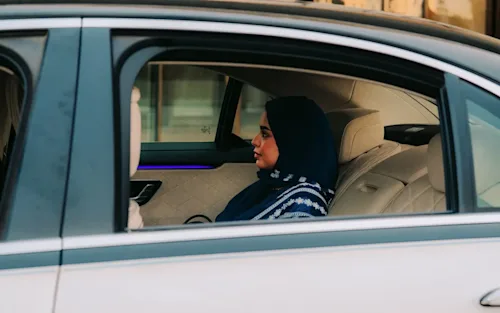 A woman in a headscarf facing forward shot through the open window of a Blacklane Mercedes EQS.