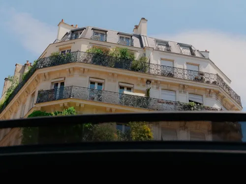 Shot of the upper floors of a Parisian building through the sunroof of a luxury vehicle.