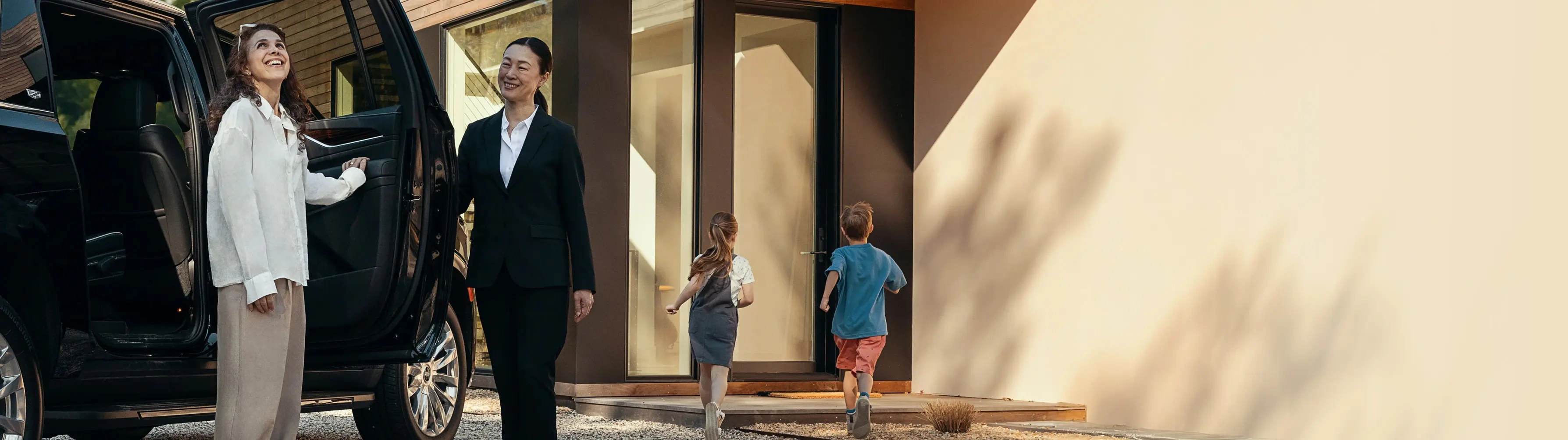 A chauffeur in a suit opens the door of a Mercedes-Benz van for a woman and her young children.