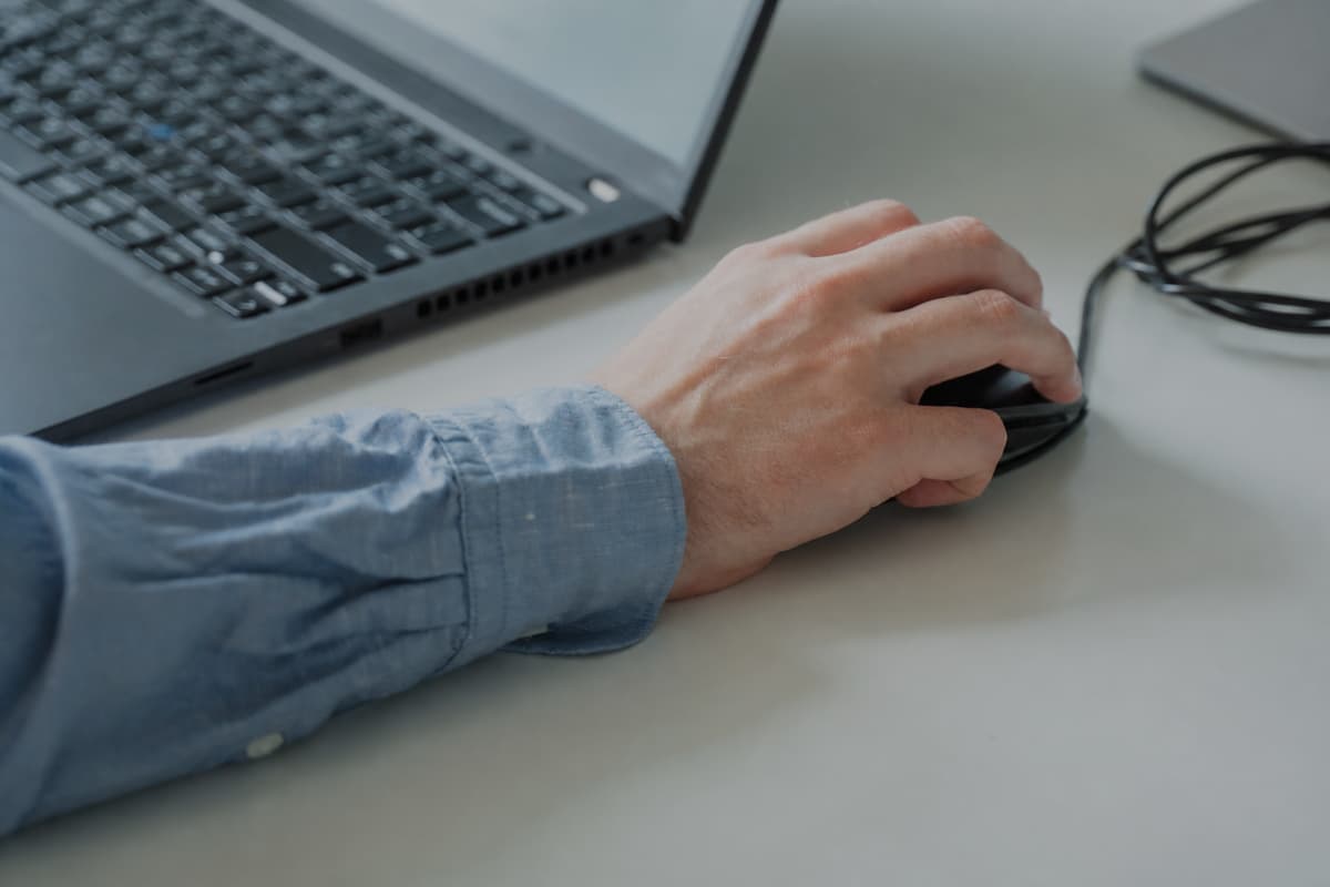 Someone's hand using a computer mouse next to a laptop.