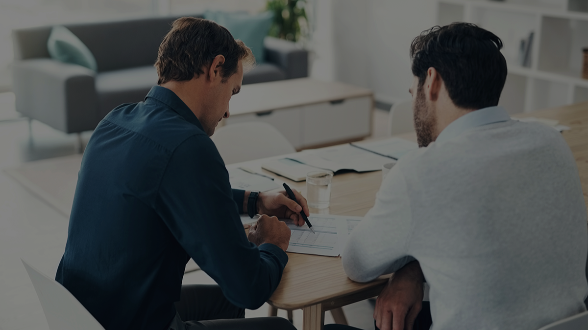 Two men sitting at a table looking over a spreadsheet.