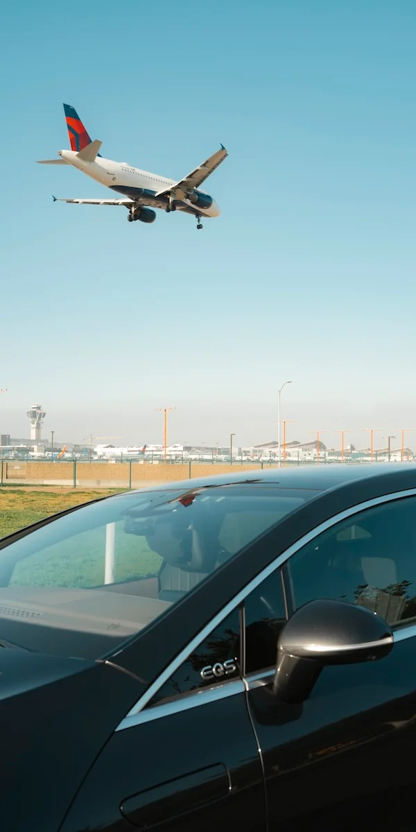 A airplane is about to touch down at an airport with a Blacklane Mercedes limo in the foreground beneath it.
