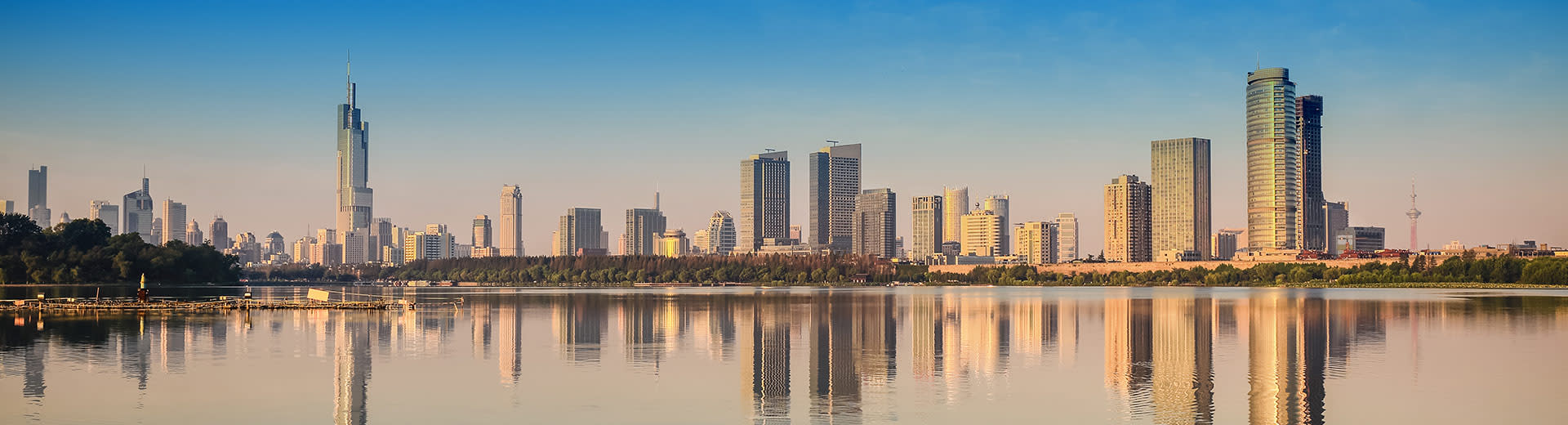 Die weitläufige Skyline von Nanjing sitzt an einem klaren und sonnigen Tag hinter ruhigem Wasser.