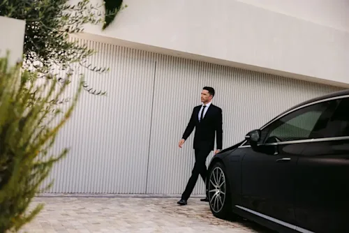 A Blacklane chauffeur walking around a Mercedes EQS limo outside a house.