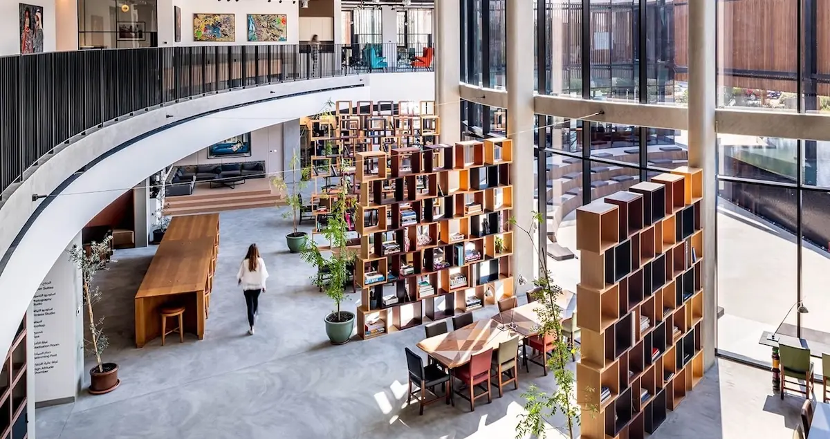 Shot of the open coworking area in Nasab private members club in Dubai, showing bookshelves and a woman walking.