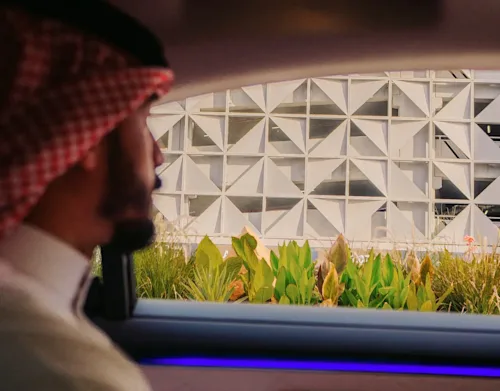 A man in traditional Saudi dress looks out the backseat window of a Blacklane limo at a modern building.