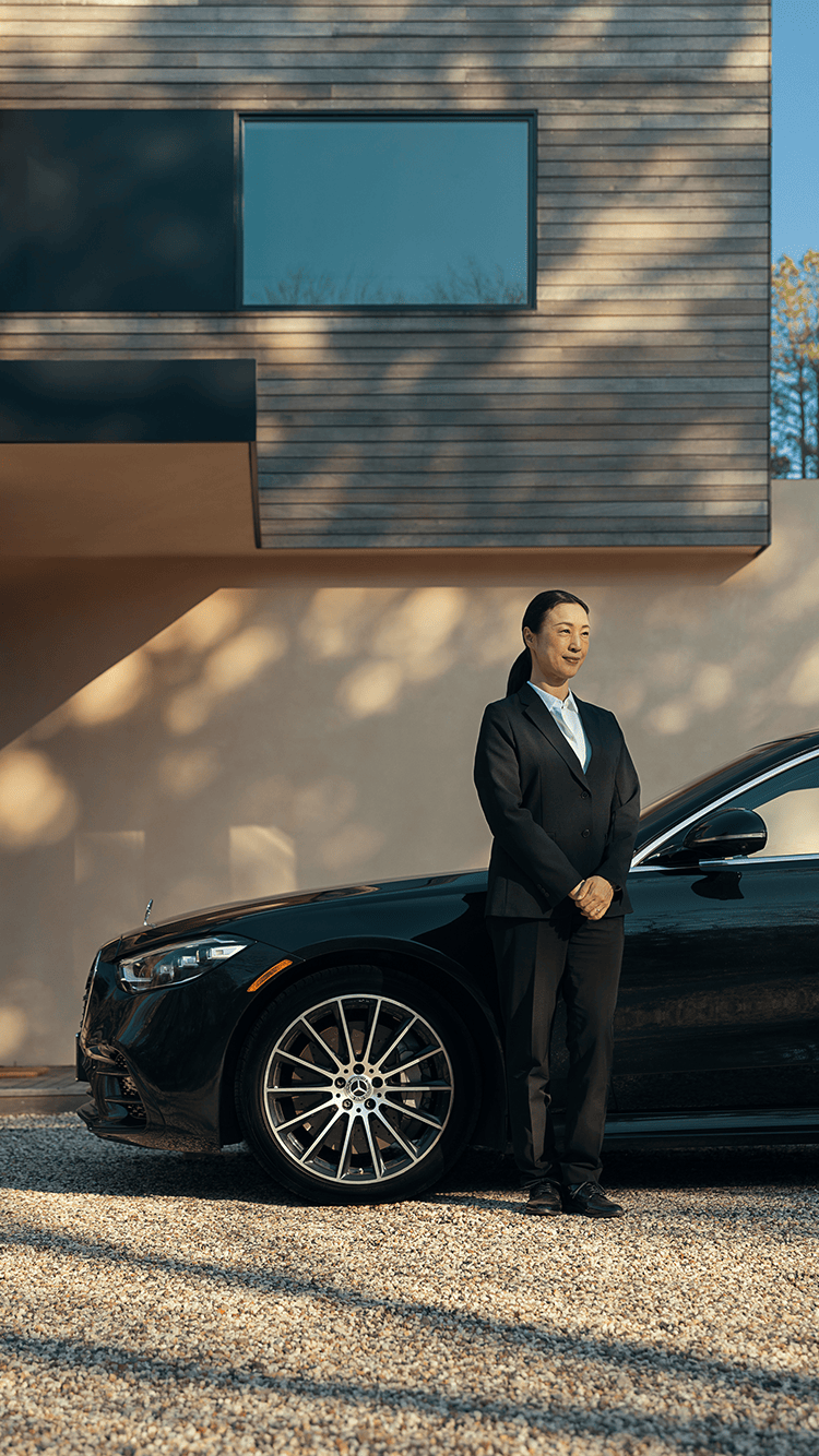 A chauffeur waits paitiently by a stylish car.