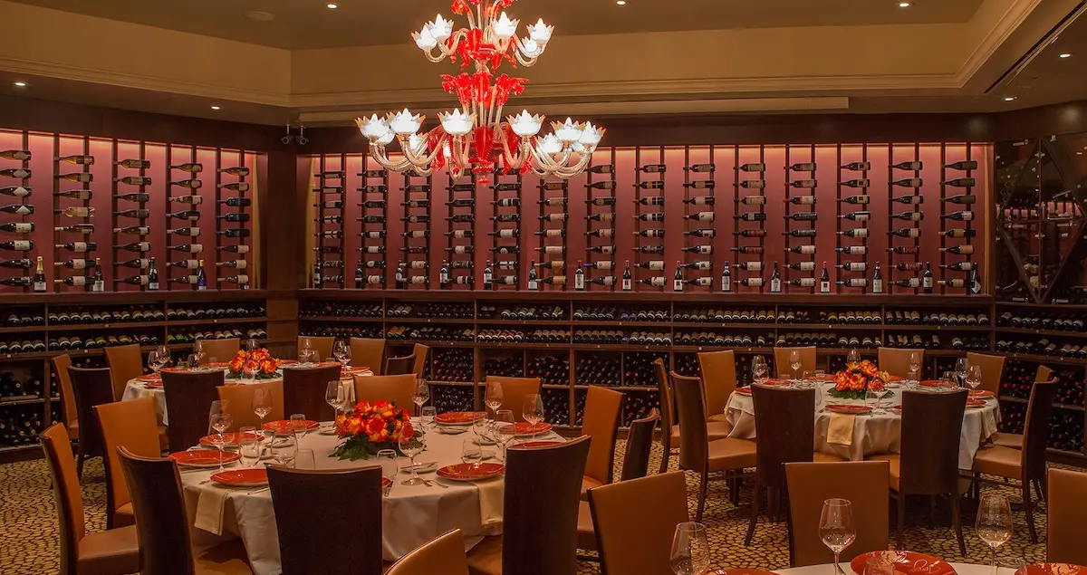 Shot of the Wine Cellar private dining room in Tony's restaurant Houston, showing circular tables set with silverware and hundreds of bottles in cases on the walls.
