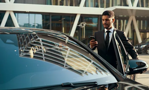 A Blacklane chauffeur opening driver door while checking his phone.
