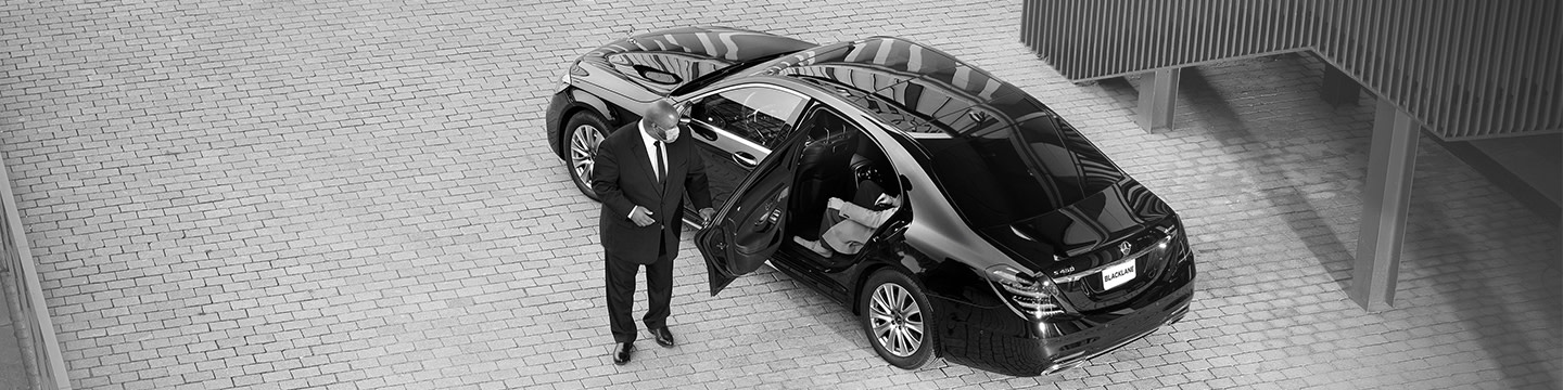 Real Blacklane chauffeur Jeffrey wears a suit and mask as he opens the door for his guest to step out of his Mercedes.