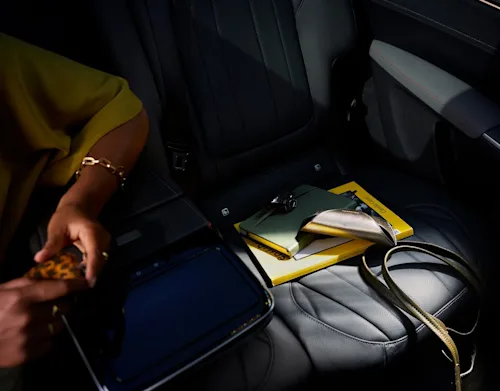 A female passenger sits in the luxury backseat of a Blacklane limousine beside her clutch bag and a book.