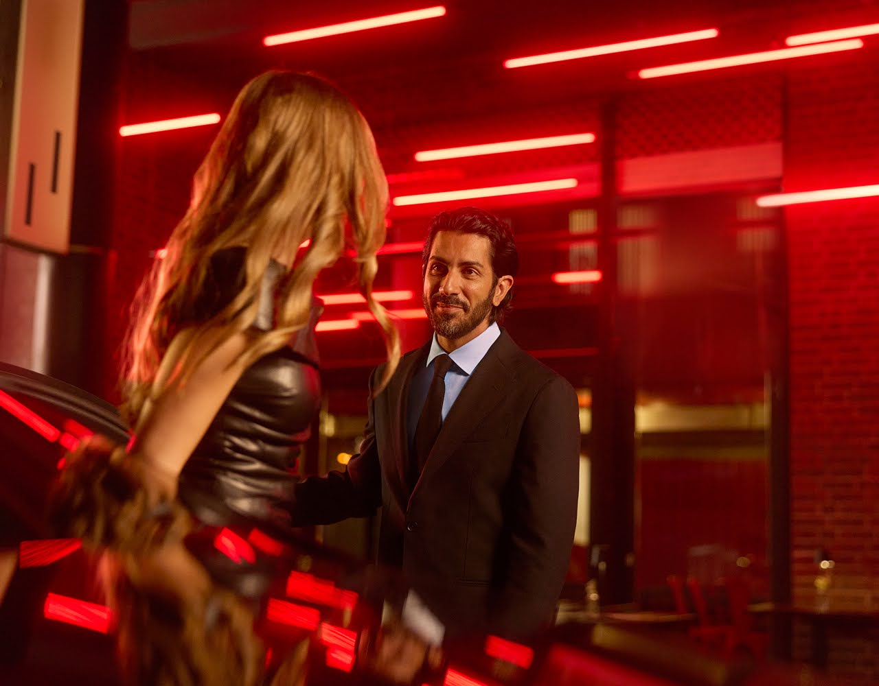 A chauffeur greets a glamourous woman as she exits a Blacklane limo in front of a venue.
