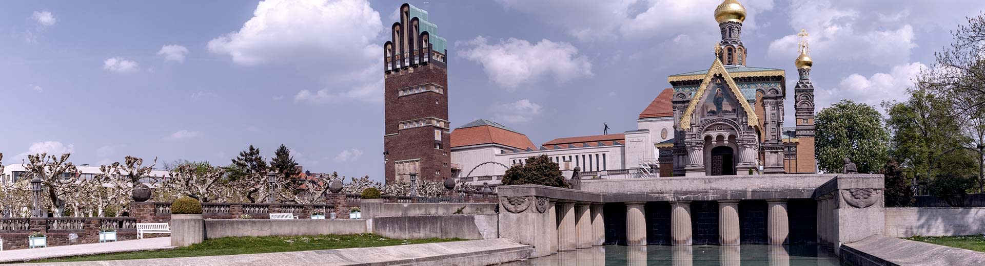 The historic churches and buildings of Darmstadt sit next to a canal on a clear and sunny day.