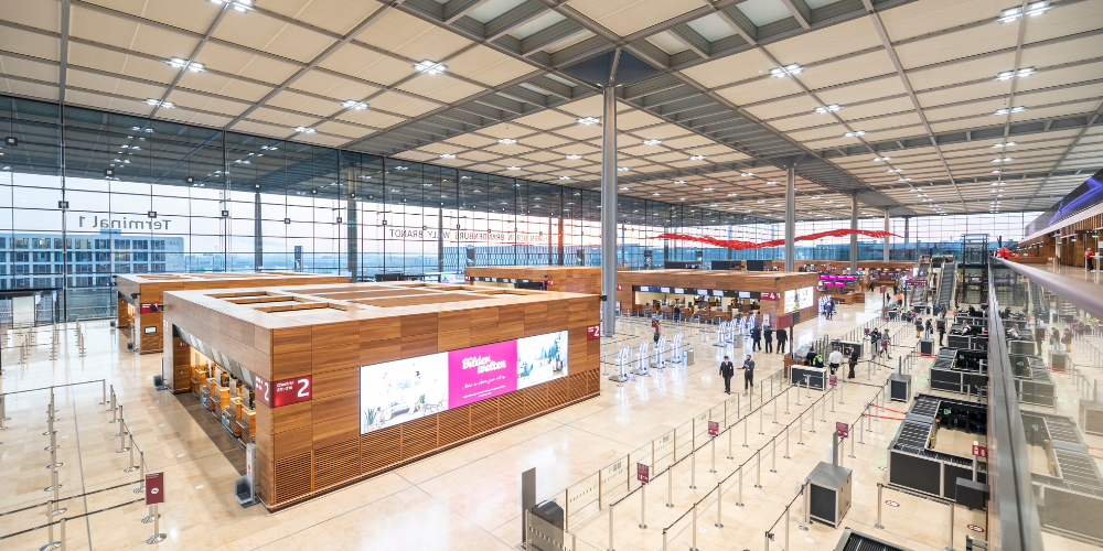 Interior of Berlin Brandenburg Airport with check-in counters and passengers.