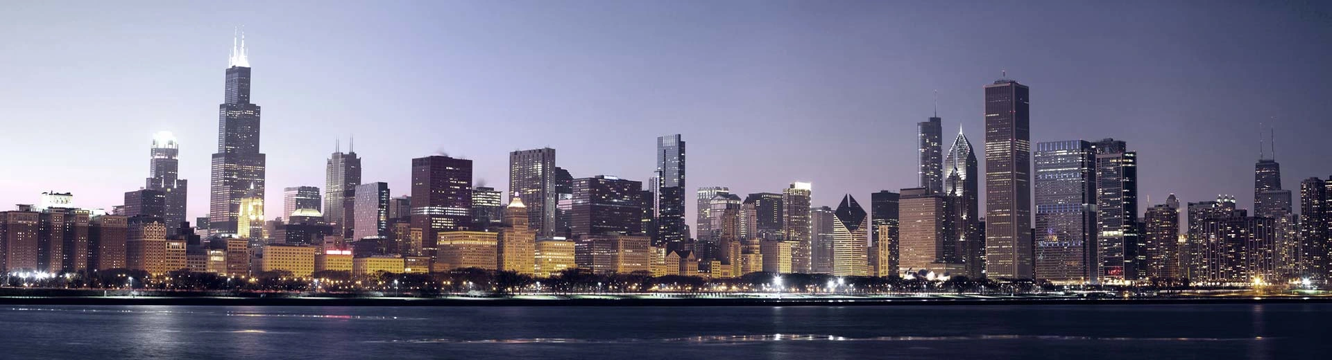 The skyline of Chicago lights up the sky above it, many tall buildings are silhouetted. 