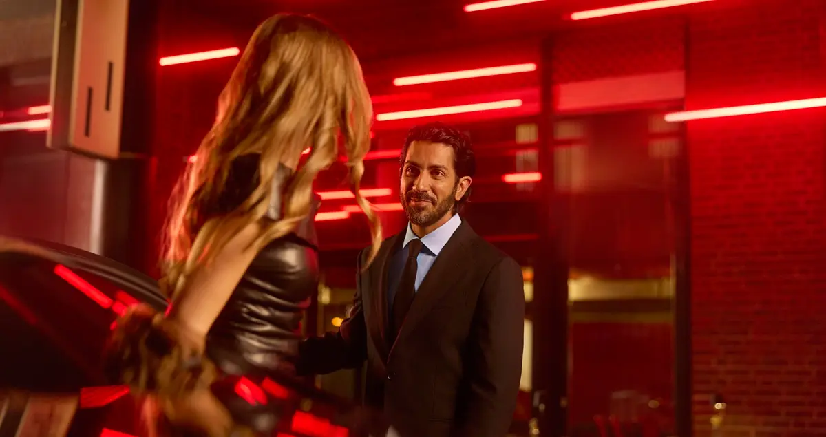 A glamourous woman leaves a Blacklane limo outside a restaurant as a suited chauffeur holds the door open for her.
