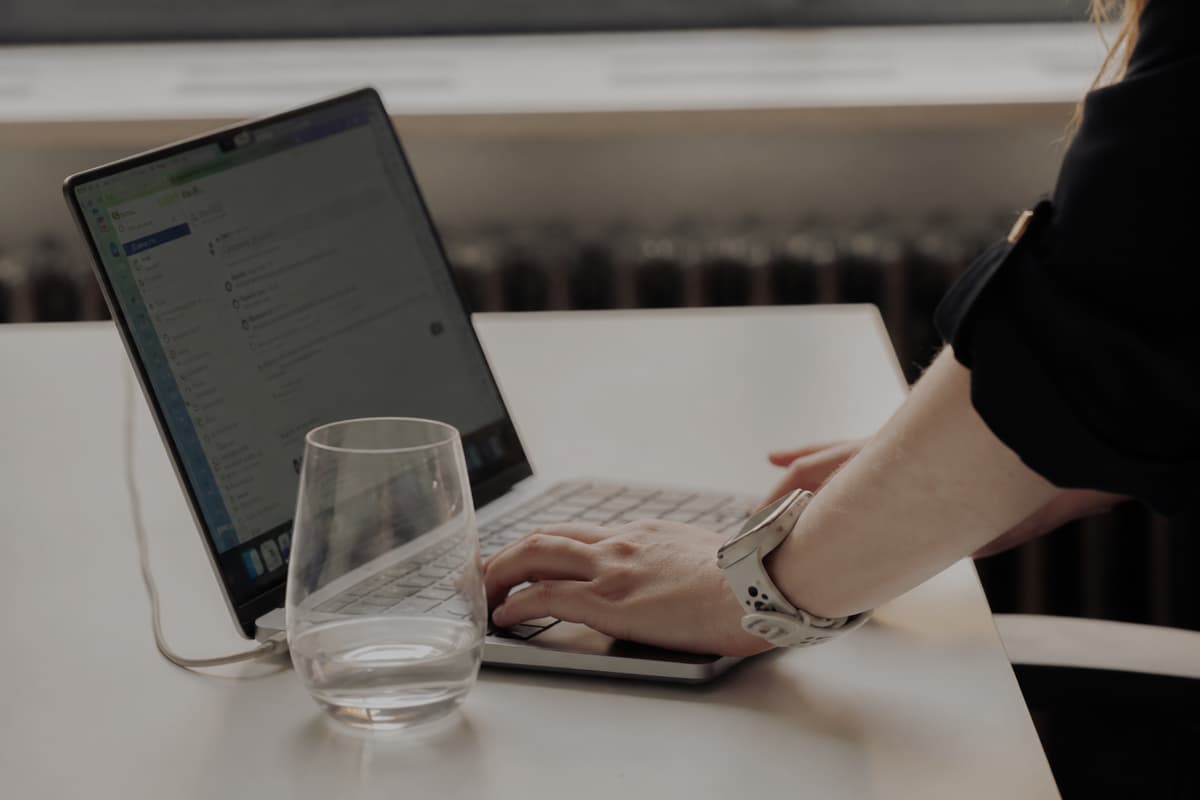 A woman's hands using a laptop on a table with a glass of water.