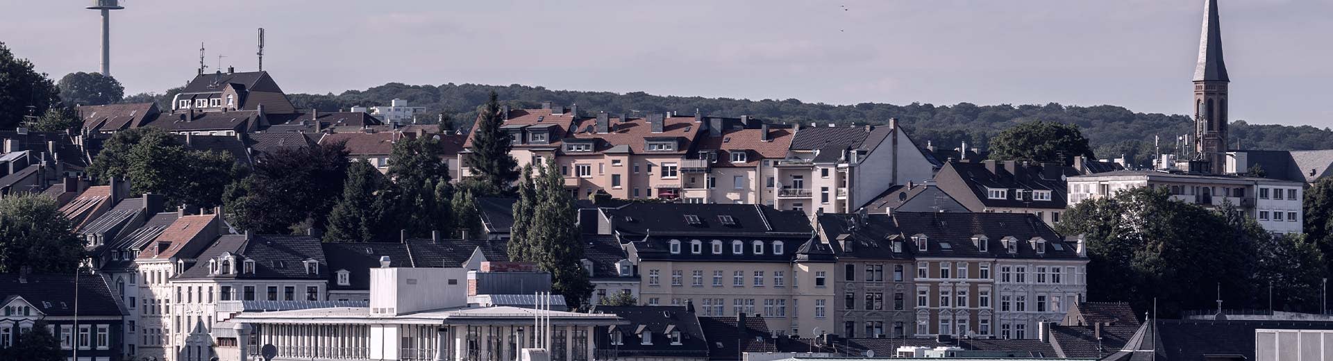 Un mélange de bâtiments résidentiels typiques de Wuppertal au premier plan est contrasté par des collines vertes au loin.