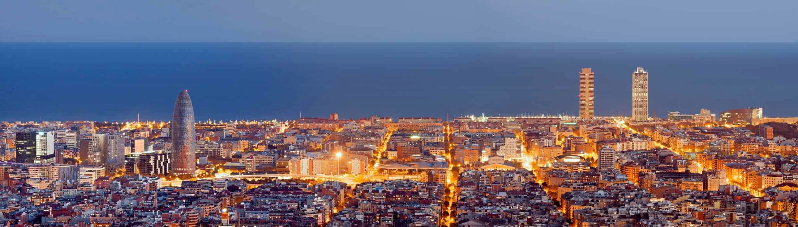 The skyline of Barcelona at night, with the sea in the background.