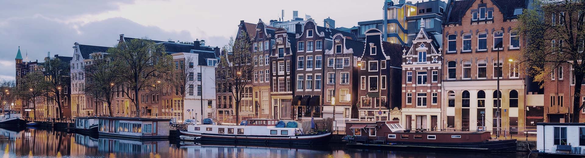 Houseboats parked alongside the canal with a strip of the Dutch style houses behind it.