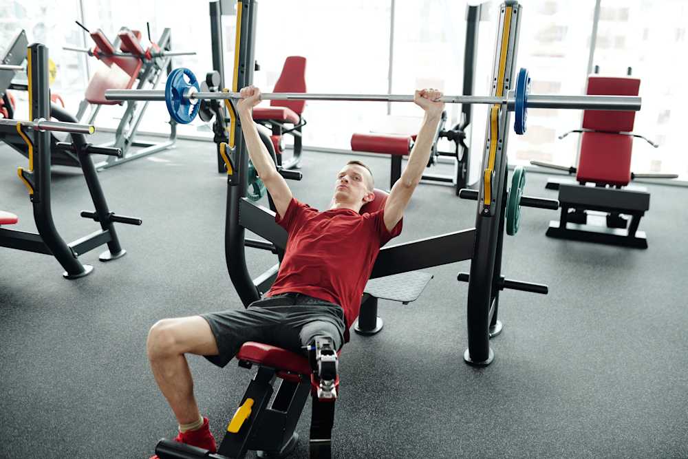 Man with a prosthetic leg in the gym exercising. He is using a bench press machine.