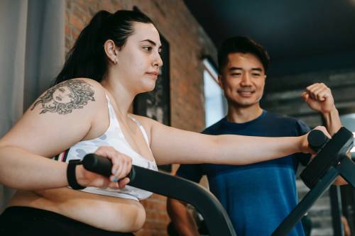 Client exercising using an elliptical machine in the gym with her PT