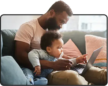 Father and toddler looking at a laptop together on a couch