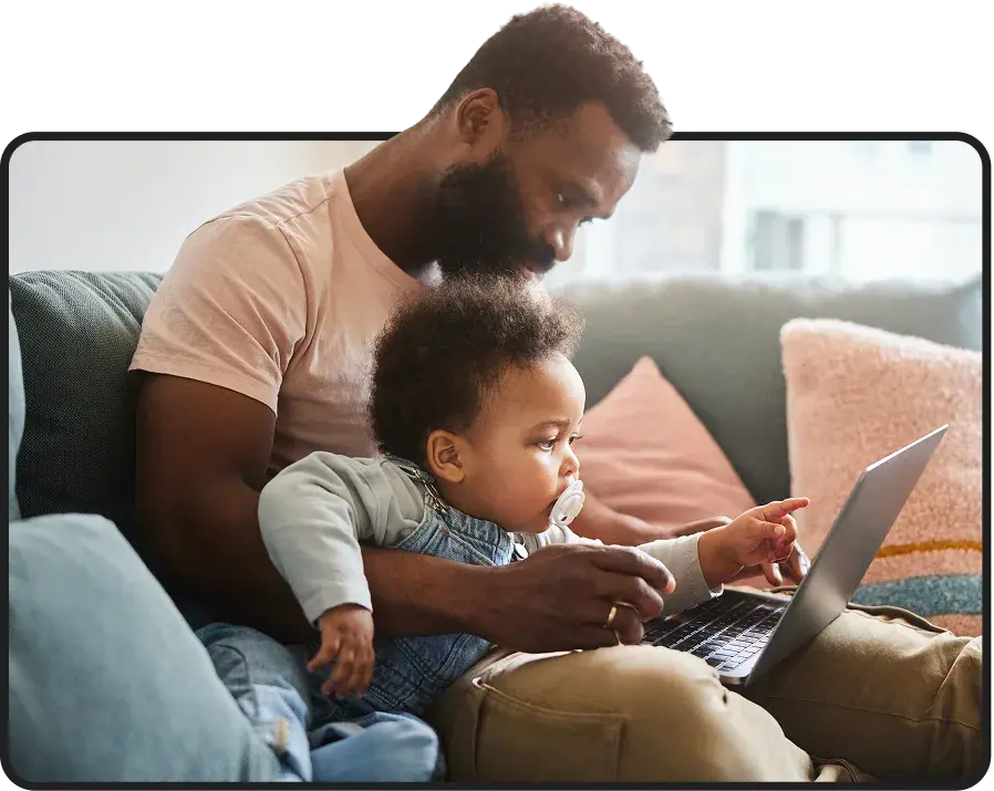 Father and toddler looking at a laptop together on a couch