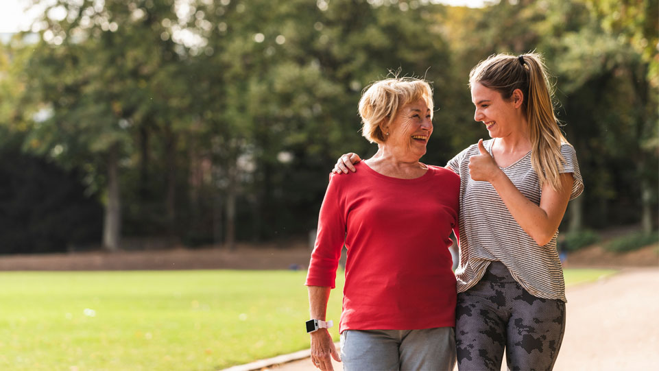 An older woman and a younger woman walking together outdoors, smiling.