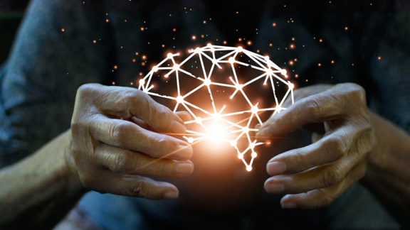 A person holds a glowing digital brain model with interconnected dots and lines.