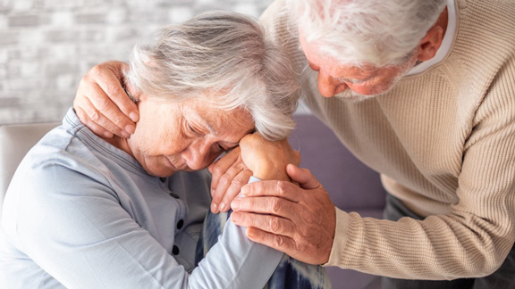 Elderly man consoles an upset elderly woman, gently holding her