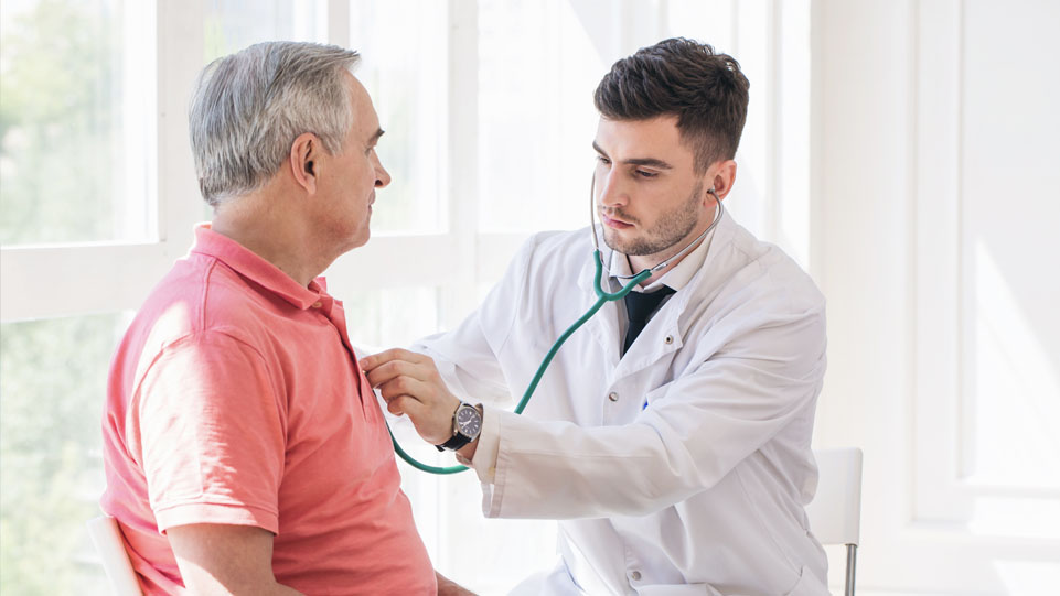 A male doctor examining an older male patient with a stethoscope.