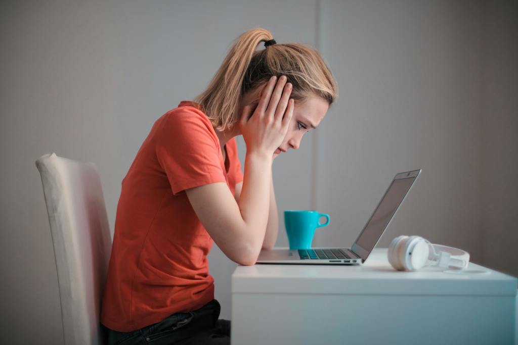 A woman touching her ears with her hands while she's sitting in front of her laptop