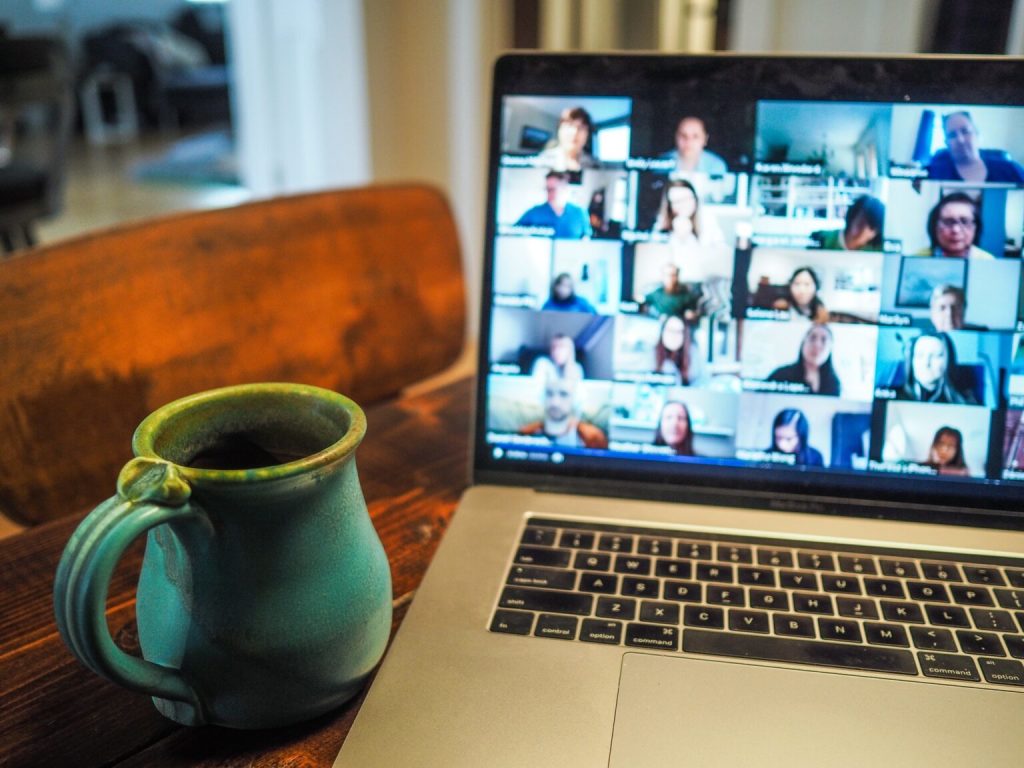 A mug and a laptop on a table, an online meeting is showed on the screen