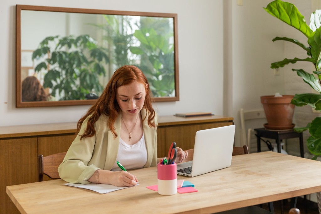 Young Woman Sitting at the Desk with a Laptop and Writing a Resignation Letter
