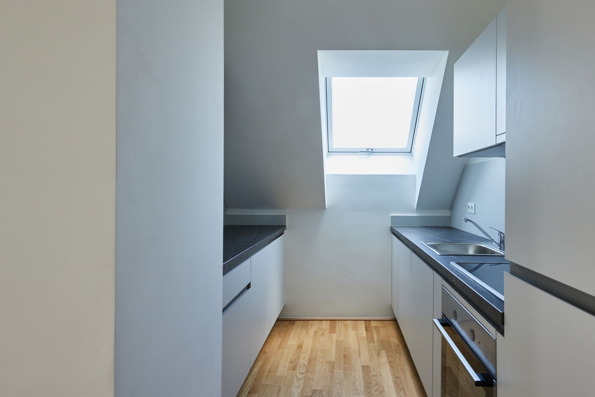 Blick durch die Tür in eine Küche, welche sich in einer Dachschräge mit Fenster befindet.