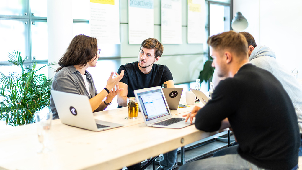 a group of people sitting around a table in an office, working