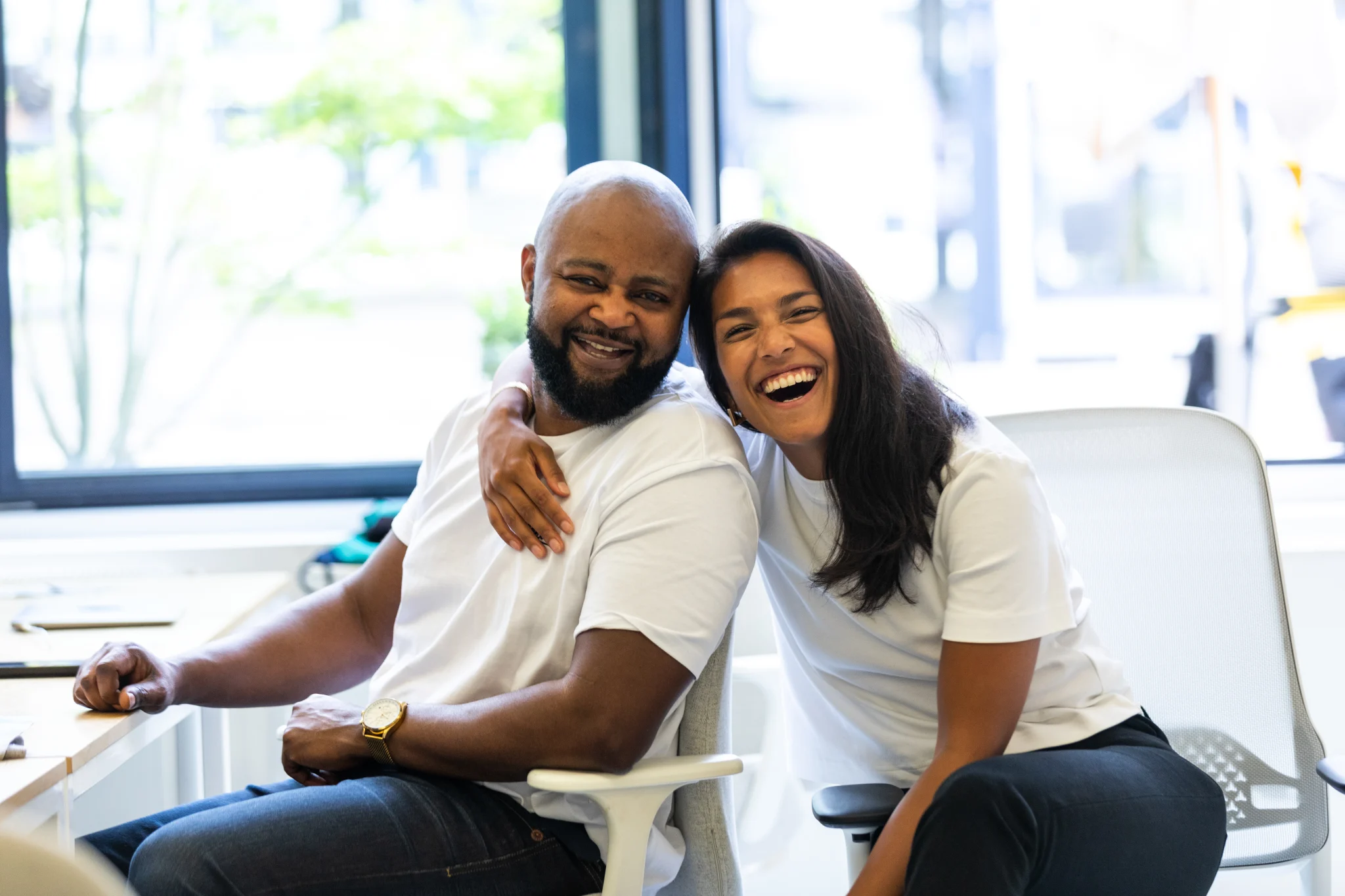 Two Personios sitting at their desks, smiling and hugging