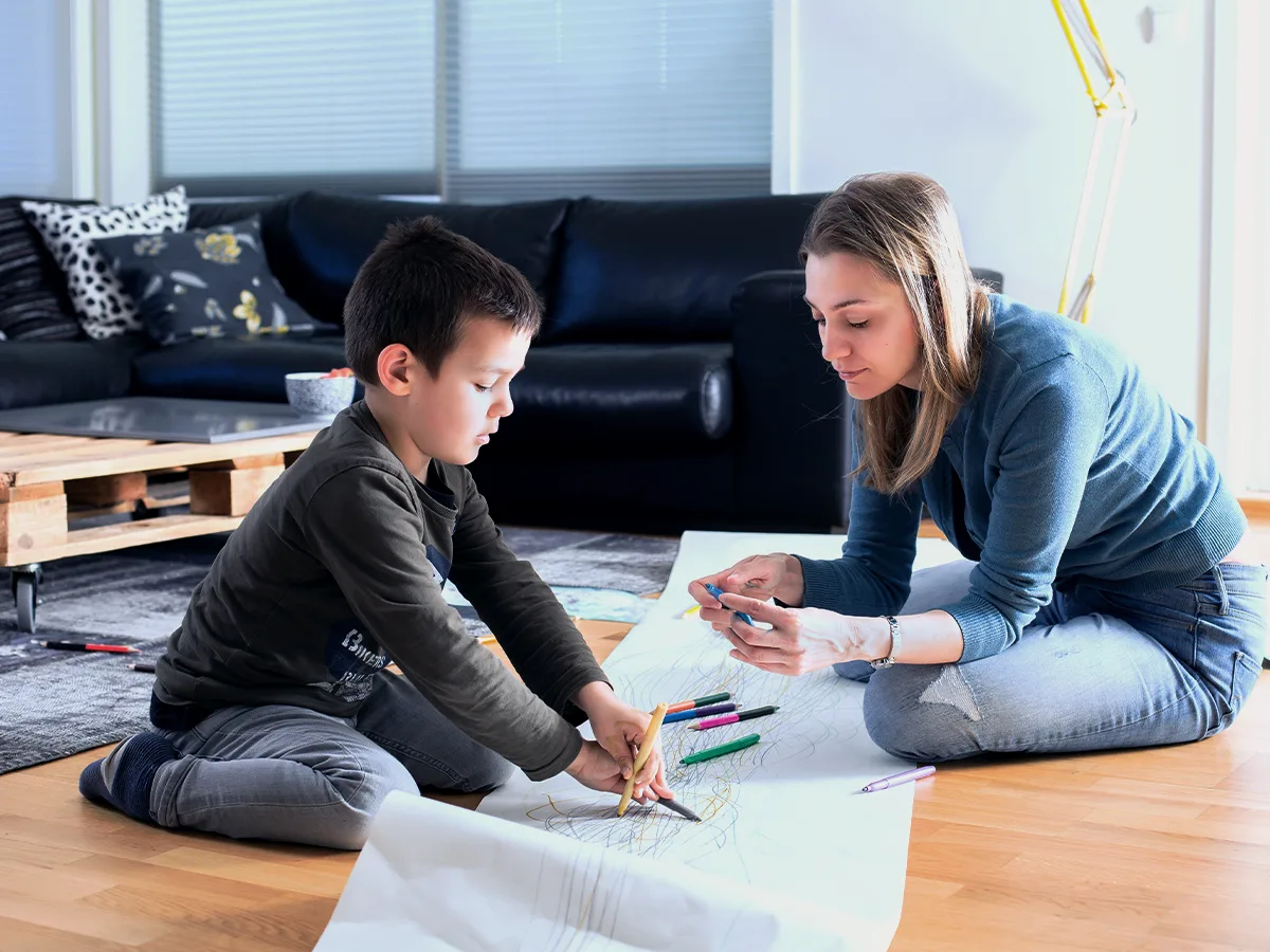 10 ways to help your grade-schooler cope with stress. A parent and child draw on paper on the floor. 